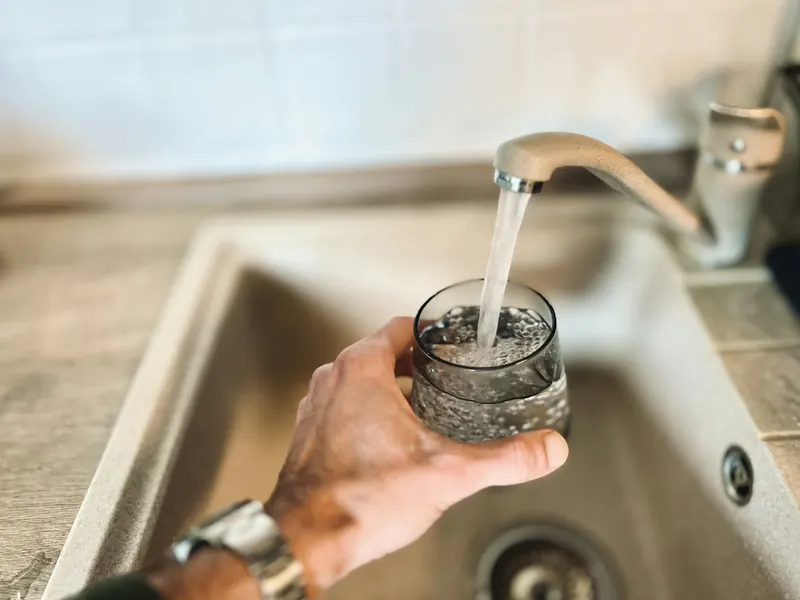 A hand filling a drinking glass from a kitchen faucet
