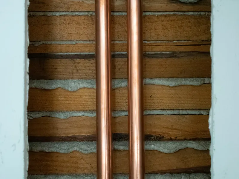 Two copper water pipes running up through an opened wall