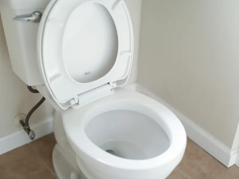 A white two-piece toilet with its seat raised and a supply line at the wall