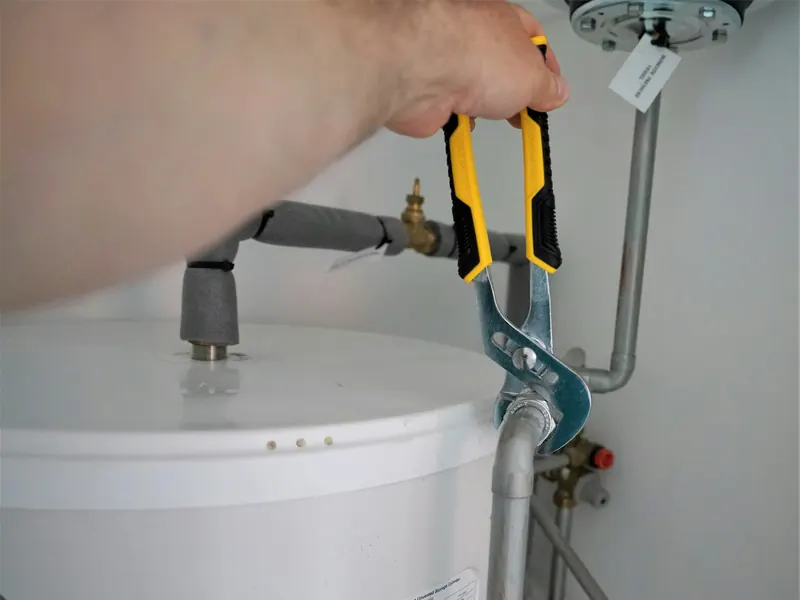 A plumber's wrench on the supply fittings at the top of a tank water heater
